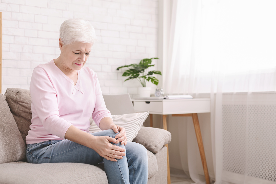 Health problems of old age. Senior woman suffering from pain in leg, massaging her knee at home, empty space